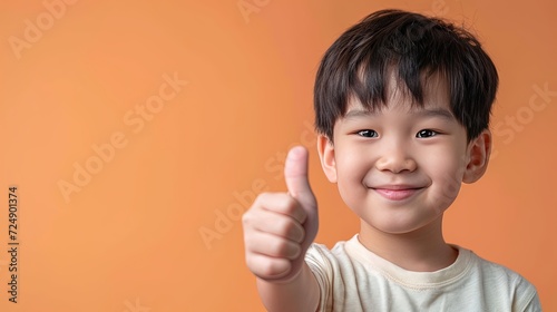Asian 7 years old boy happily smiles and shows thumbs up on yellow background. Sign everything is fine, approval