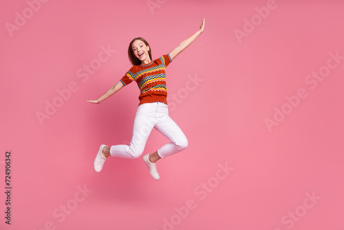 Full length photo of excited cute girl raise arms jumping flying empty space isolated on pink color background