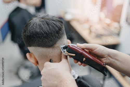 Closeup master barber hairdresser does hairstyle with hair clipper and comb. Concept banner Barbershop for man