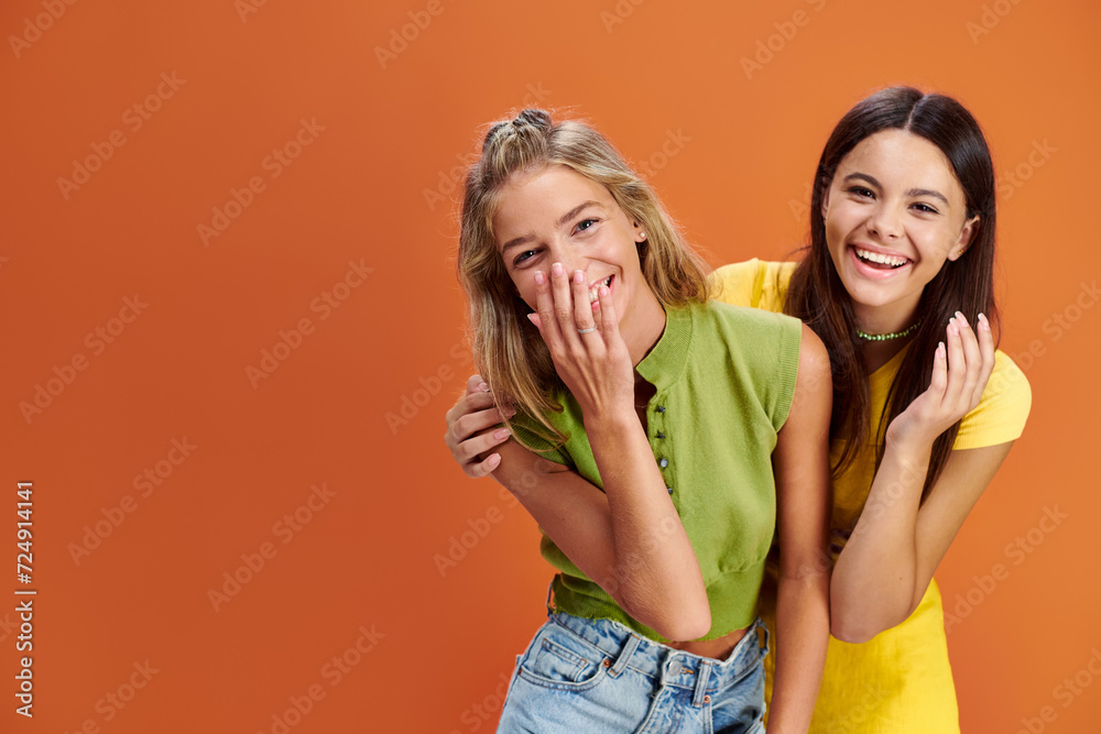 joyous adorable adolescent girls hugging and smiling at camera on orange backdrop, friendship day joyous adorable adolescent girls hugging and smiling at camera on orange backdrop, friendship day