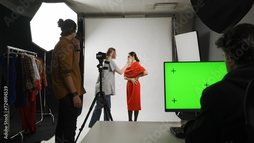 Backstage of model and professional team in the studio. Stylist assistant fixing look of model on set, editor at the desktop chroma key green screen.