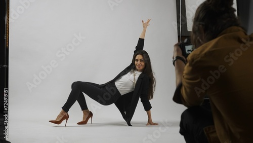 Backstage of model and professional team in the studio. Full length of attractive model in suit posing on the floor, photographer taking photos.