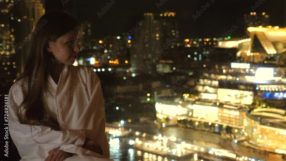Contemplative woman looking at night city lights from high-rise building. Urban lifestyle and solitude. Contemplative woman looking at night city lights from high-rise building. Urban lifestyle and solitude.