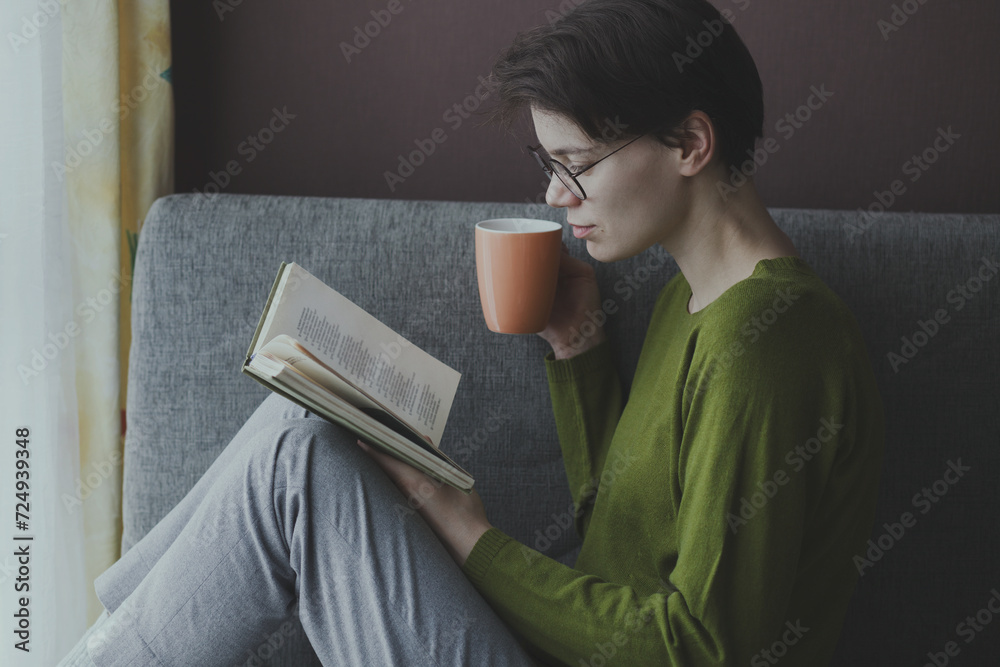 Obraz premium Young woman reading book and drinking coffe at home, relax or education concept