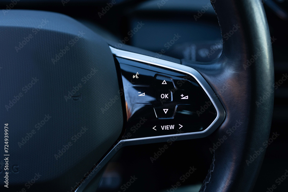 Close-up view of car interior. View of steering wheel of car control music. Volume button of car radio on steering wheel. Turns up the volume of the music in the car.