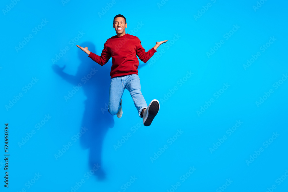 Full size portrait of active cheerful young man jump arms hold empty space isolated on blue color background