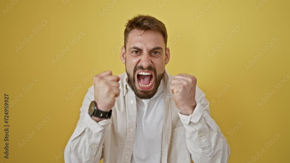 Angry young hispanic man, stressed and screaming, standing against a yellow isolated background. portrait of furious expression caught on camera.