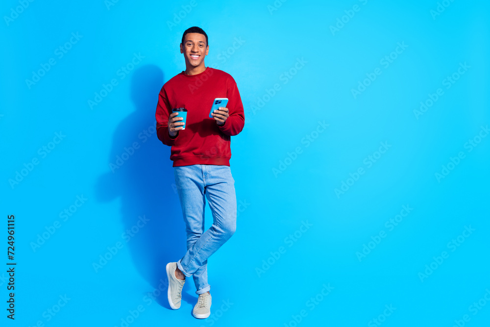 Full body portrait of positive handsome guy use smart phone drink coffee empty space isolated on blue color background