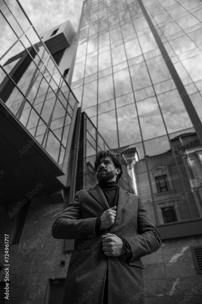 Fototapeta premium Image of a single bearded man in jacket posing behinde higher building. Black and white image.