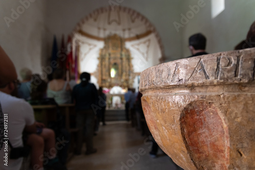 Vista interior de una iglesia católica durante la misa con la pila bautismal en primer plano.