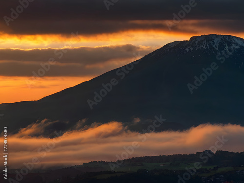 Background, Mountains at sunset over a dark mountain. Colorful sunrise with clouds over the hill. The sun hides behind a cloud in the daytime sky