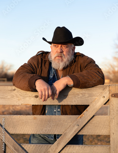 Shallow depth of field outdoor portrait of bearded old rancher cowboy focused on face while leaning on a fence looking to side in the distance in Yellowstone County Montana photo