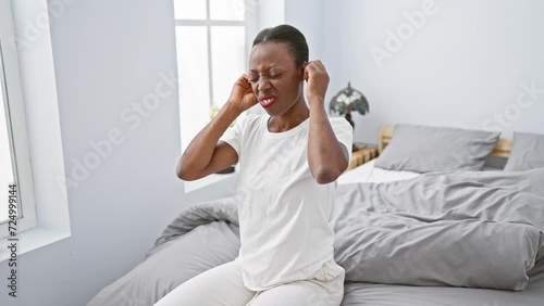 Annoyed african american woman in bedroom, covering ears with fingers, lying on bed, unable to relax amid deafening noise photo