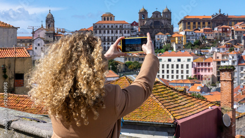 Blonde tourist woman with curly hair takes a photo with the mobile phone in the city of Porto, Portugal
