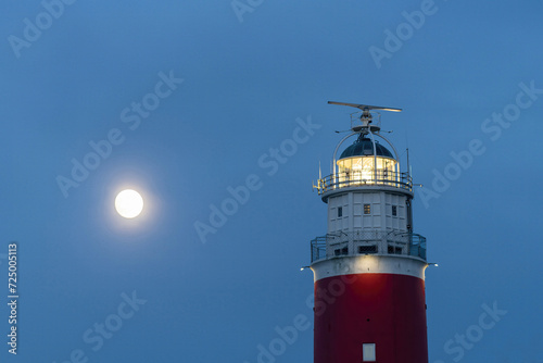 Low angle close up view of light of historical red lighthouse and rising full moon on the island of Texel, the Netherlands during dusk