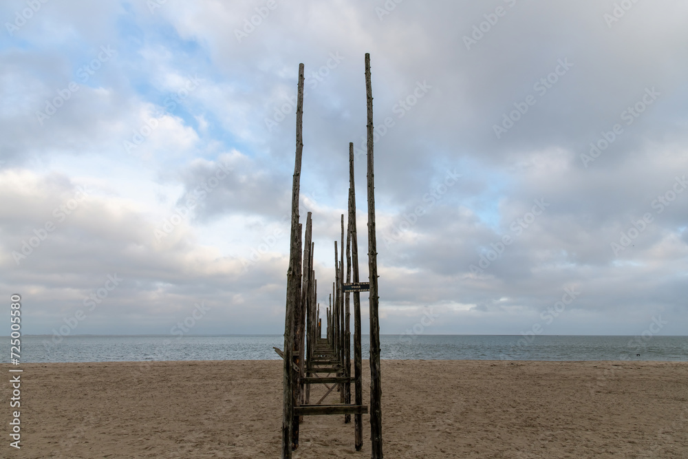 Low angle  horizontal view of a characteristic boat pier with long wooden poles on the island of Texel in the Netherlands with dark clouds gathering over sea (sign: prohibited for unauthorized people)