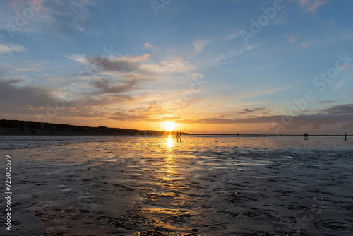 Low angle view of patch of sand along the beach at low tide along the coastline of Texel Island  the Netherlands during sunset with mix of dramatic clouds and clear skies  sun reflected in water pools