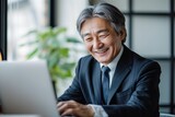 パソコンに向かって笑う年配の日本人男性（打ち合わせ・商談・リモート会議）