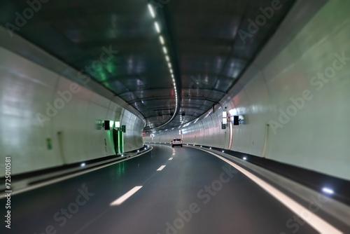 View over the length of a brightly lit modern tunnel with blurry tunnel and road deck becoming more focused at end of tunnel with distancing white car