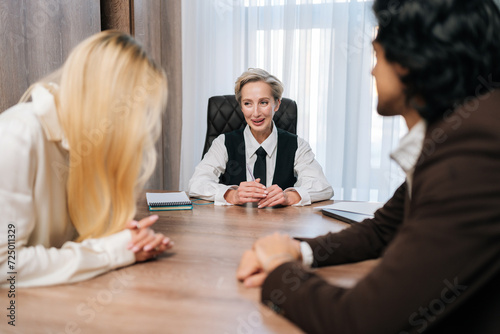 Group of cheerful business people having conversation sitting at desk in conference room, gathered for project discussion, looking positive, enjoy communication and teamwork together in office.