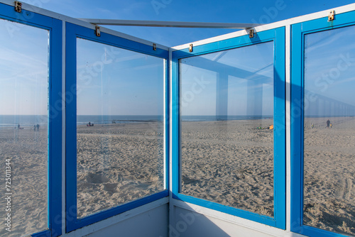 View over the beach and sea of Texel island in the Netherlands seen through the glass windows of a windscreen of one of the beach pavilions on the coast with some people on an otherwise empty beach photo