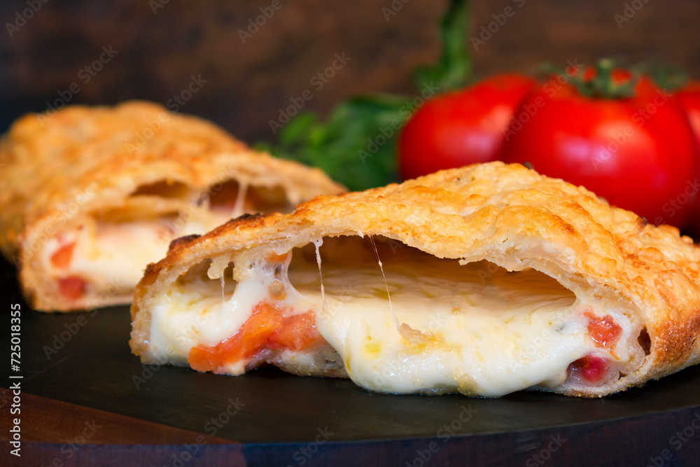 Baked cheese pastry with tomato, open with the cheese melting, on a wooden board and in the background blurred tomatoes and seasonings Baked cheese pastry with tomato, open with the cheese melting, on a wooden board and in the background blurred tomatoes and seasonings