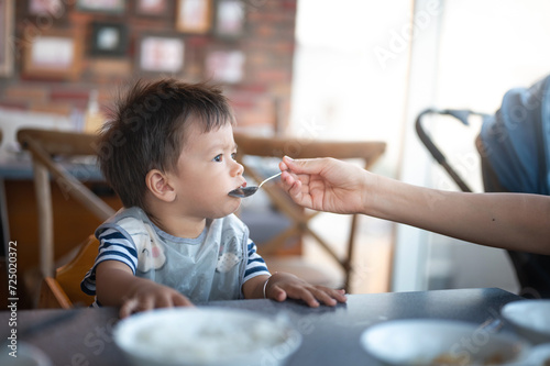 Mother feeds a hungry baby boy with soup in a restaurant