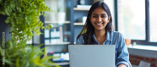 Smiling young indian woman working on a laptop, surrounded by the freshness of indoor plants photo