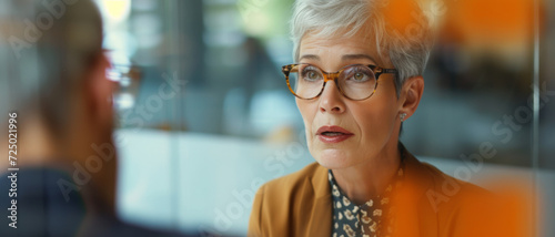 Mature businesswoman in a serious discussion, her glasses reflecting the gravity of the conversation