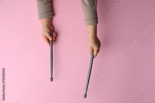 Little kid holding drumsticks on pink background, top view photo