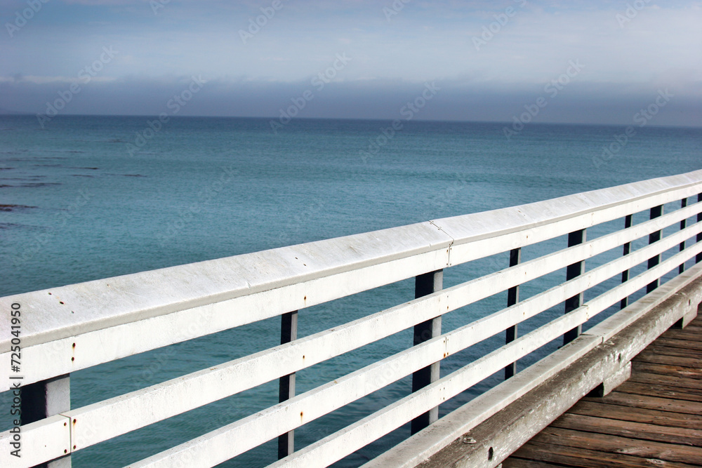 Horizontal detail of a railing of an old wooden pier overlooking a calm ocean.