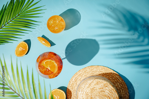 Summer refreshing cocktail aperol spritz with orange and palm leaves on a blue background with shadows, top view photo