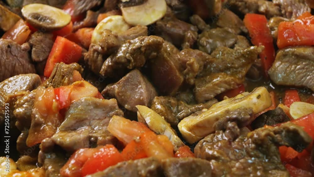 Pieces of beef in a frying pan with butter and champignons and tomatoes are mixed with a wooden spatula Pieces of beef in a frying pan with butter and champignons and tomatoes are mixed with a wooden spatula