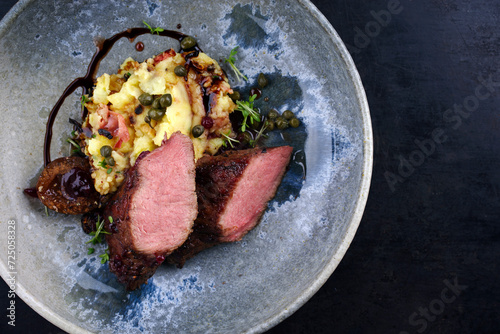 Traditionell gebratenes Wildhasen Rücken Filet mit Pflaumen, Kapern und Kartoffelsalat in Rotweinjus serviert als Draufsicht auf einem Nordic Design Teller mit Textfreiraum