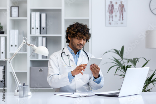 Young medical practitioner concentrated on digital tablet while working in a modern clinic. Represents healthcare technology. photo