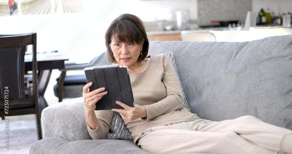 Woman enjoying using reading studying on wireless mobile tablet relaxing lying on comfortable living room sofa. Woman enjoying using reading studying on wireless mobile tablet relaxing lying on comfortable living room sofa.