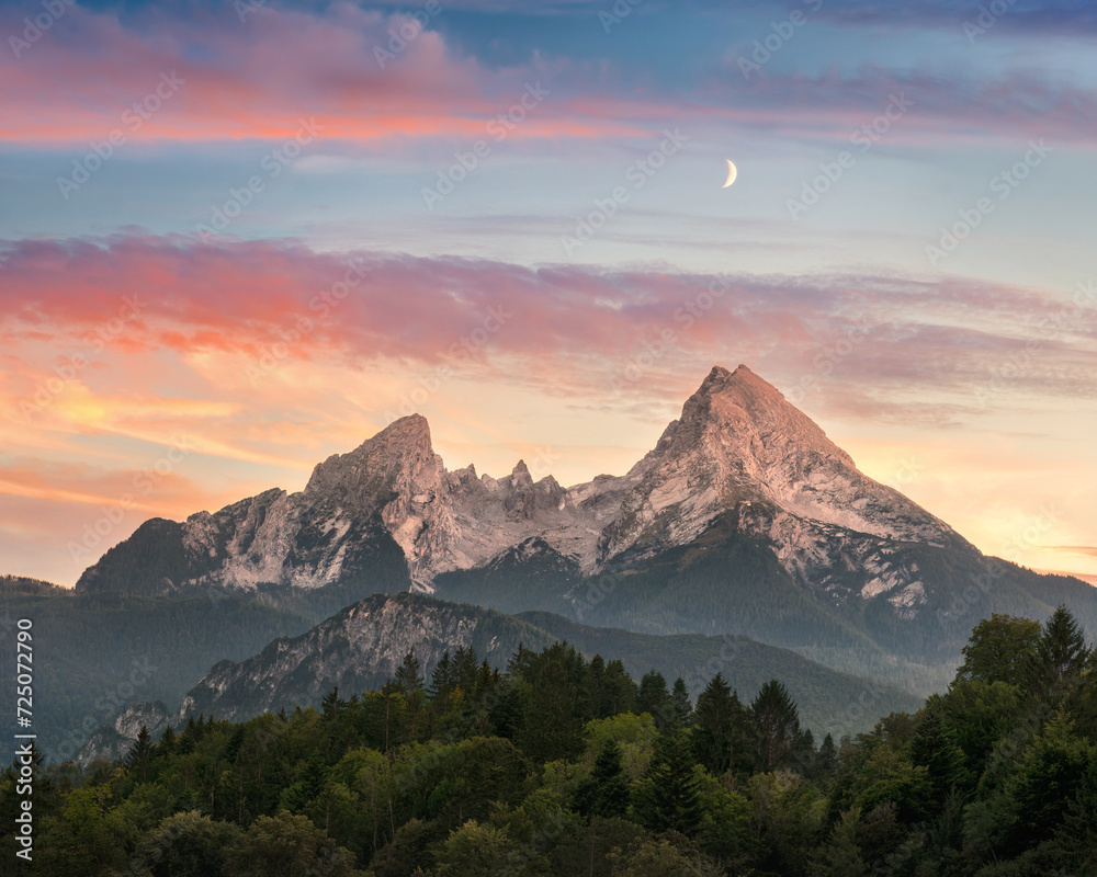 A majestic mountain formation, the Watzmann in Bavaria, Germany, with a colorful sunset sky and woodlands in the foreground