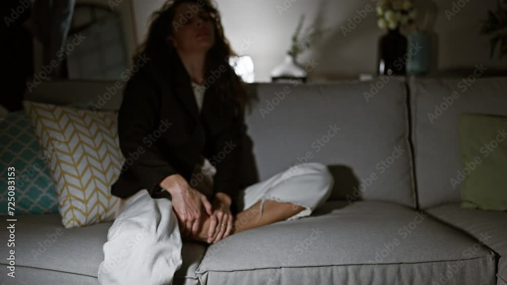 Tired young woman sitting on couch at home, relaxing in a dimly lit cozy living room Tired young woman sitting on couch at home, relaxing in a dimly lit cozy living room