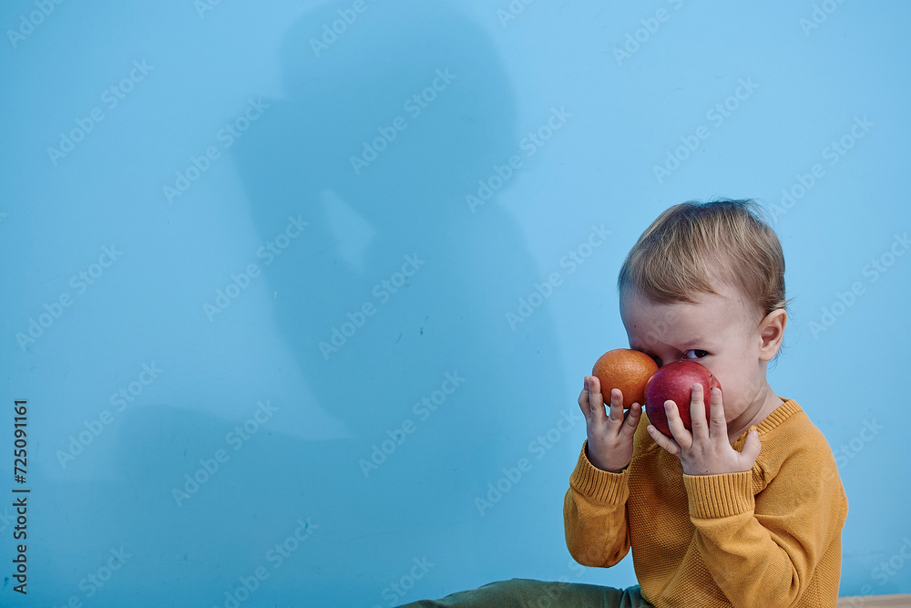 2 year old boy sitting holding red apples and closing eyes background blue wall 2 year old boy sitting holding red apples and closing eyes background blue wall