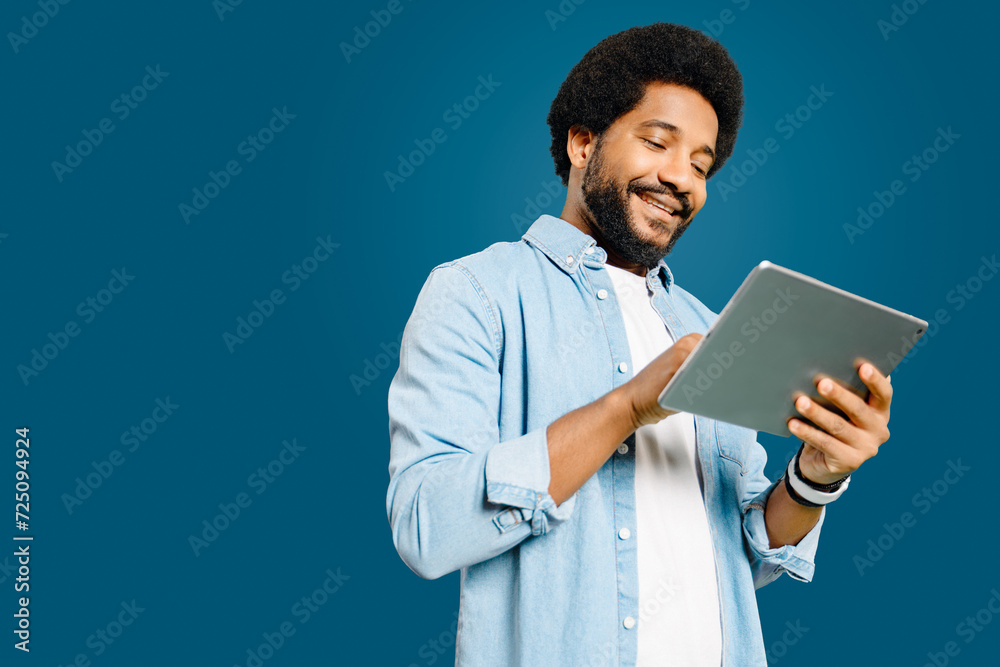 Smiling while using his tablet, the young Latin man presents a scenario where technology meets daily life, whether it's for work, study, or play, depicting the versatility of such devices, isolated