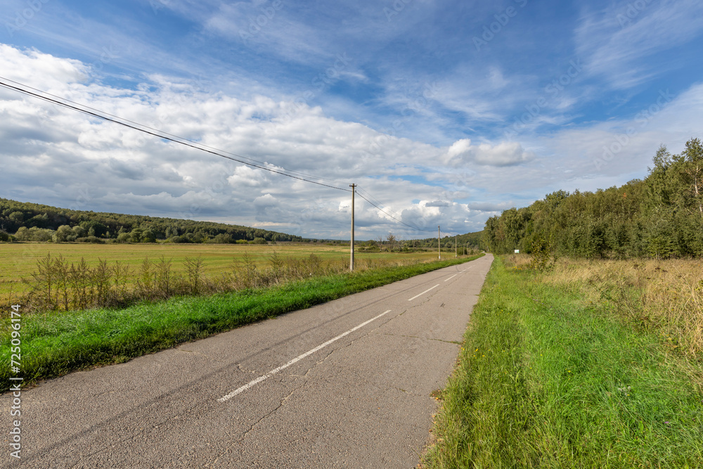 road in the countryside, bright sunny afternoon, an asphalt road along which there is an electric wire on concrete supports