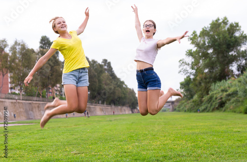 Portrait of cheerful teenage girls jumping together in summer city park. Concept of happy adolescence