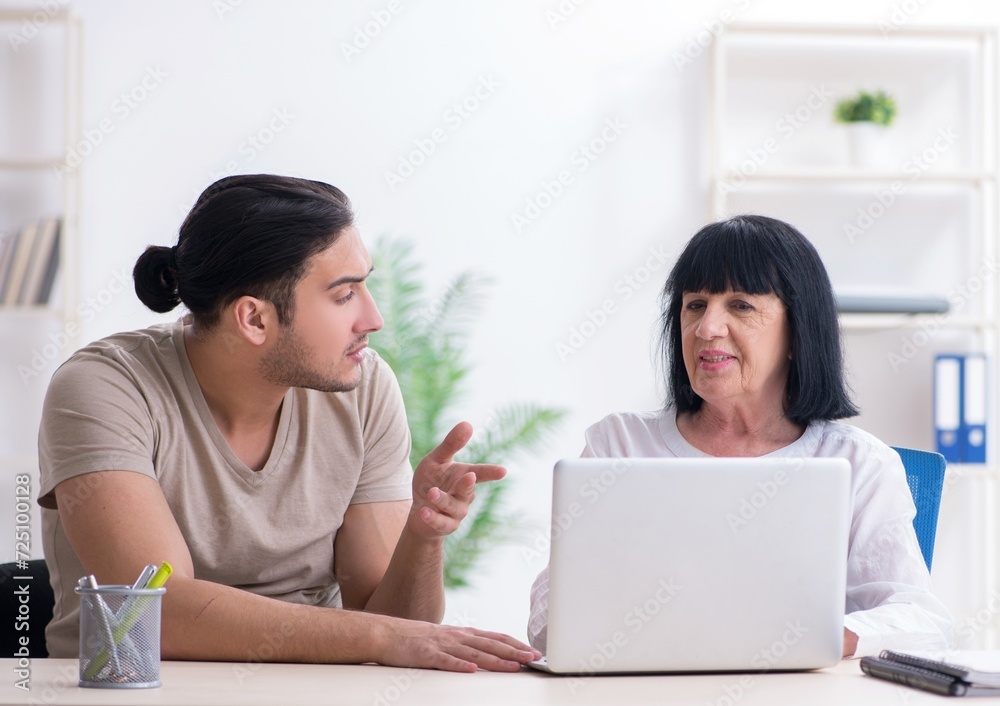 Young male employee explaining to old female colleague how to us