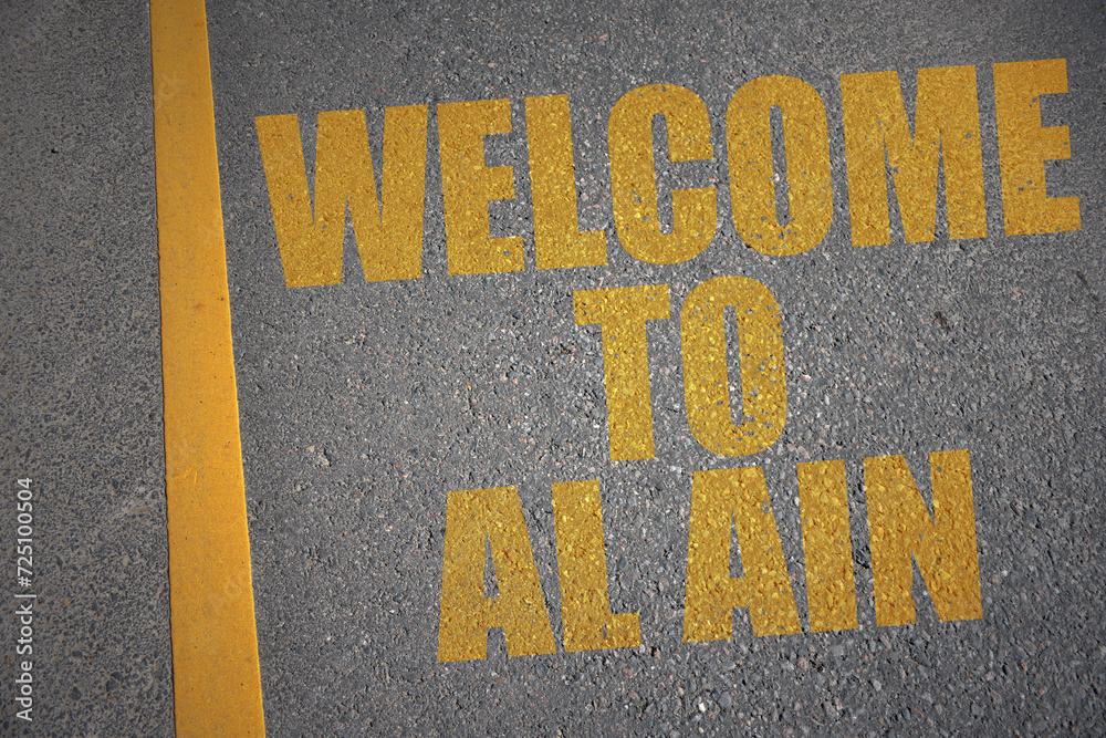asphalt road with text welcome to Al Ain near yellow line.