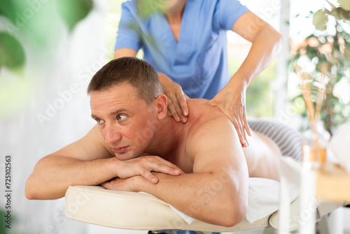 massage therapist doing a body massage to a man who lies on the couch © JackF