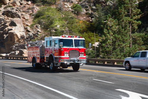 A red firetruck with emergency lights flashing passing cars as it races down a mountain road.