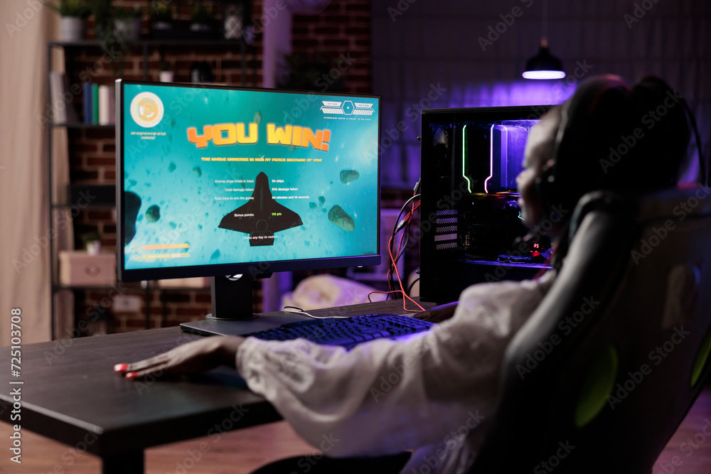 Gamer celebrating winning online multiplayer SF videogame matchup. African american woman enjoying down time at home, feeling pleased about internet gaming championship victory Gamer celebrating winning online multiplayer SF videogame matchup. African american woman enjoying down time at home, feeling pleased about internet gaming championship victory