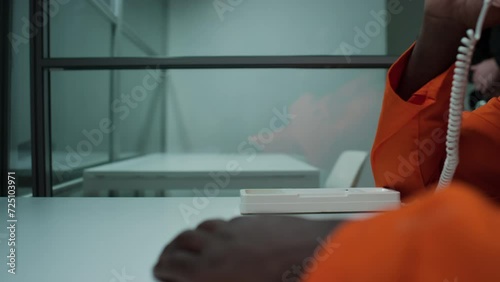Close up view of hand of unrecognizable Black inmate sitting at table in visiting room and taking landline phone for conversation photo