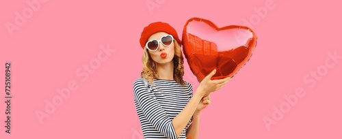 Sweet portrait of beautiful happy woman with red heart shaped balloon blows kiss