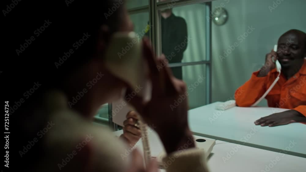 Rack focus over the shoulder shot of African American inmate smiling and speaking with family visiting him in prison Rack focus over the shoulder shot of African American inmate smiling and speaking with family visiting him in prison